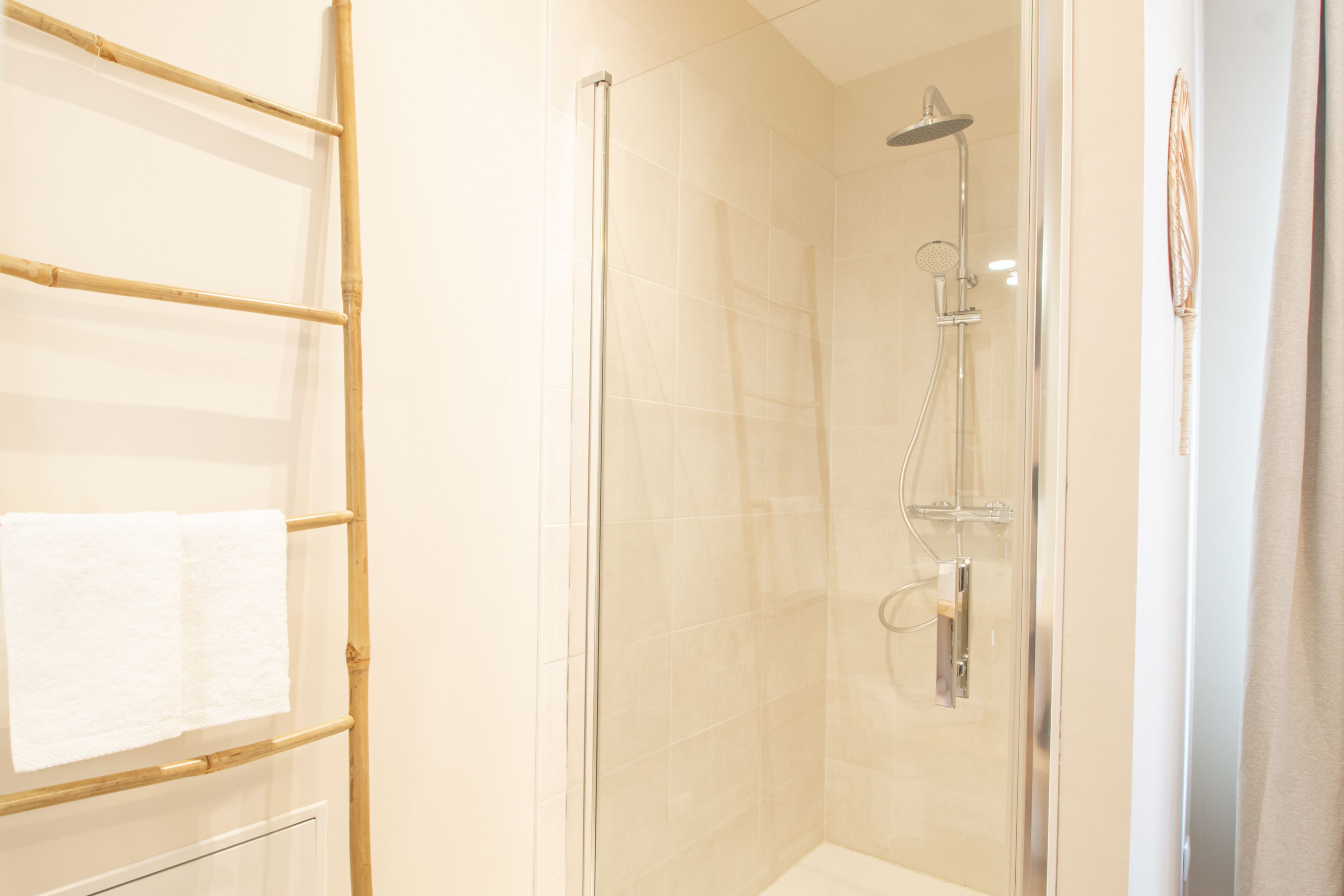 A glass-enclosed shower with a handheld showerhead and a wall-mounted faucet.