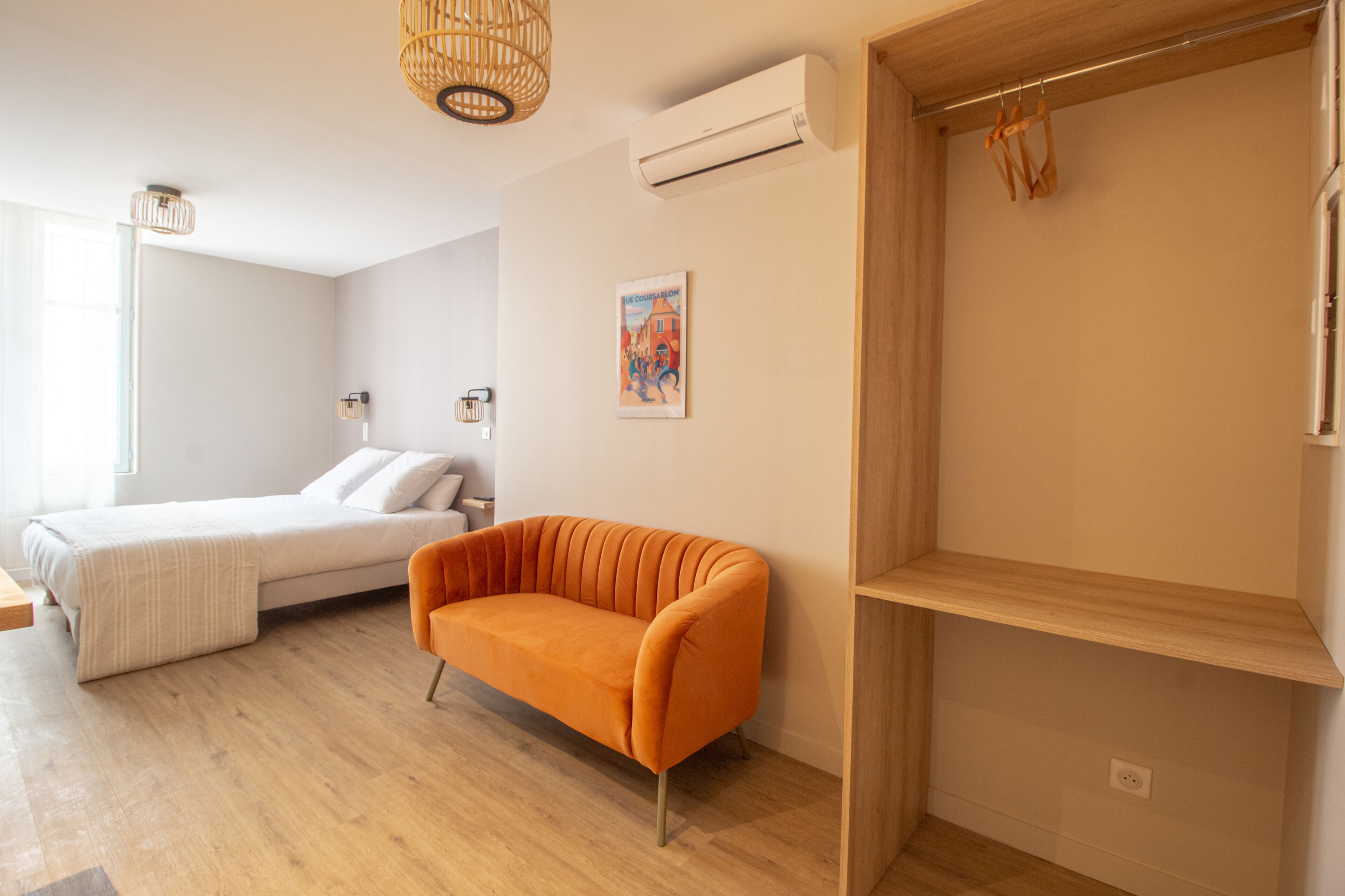 A modern bedroom with a bed, an orange sofa, a wooden shelf, and a wall-mounted air conditioner.