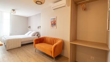 A modern bedroom with a bed, an orange sofa, a wooden shelf, and a wall-mounted air conditioner.