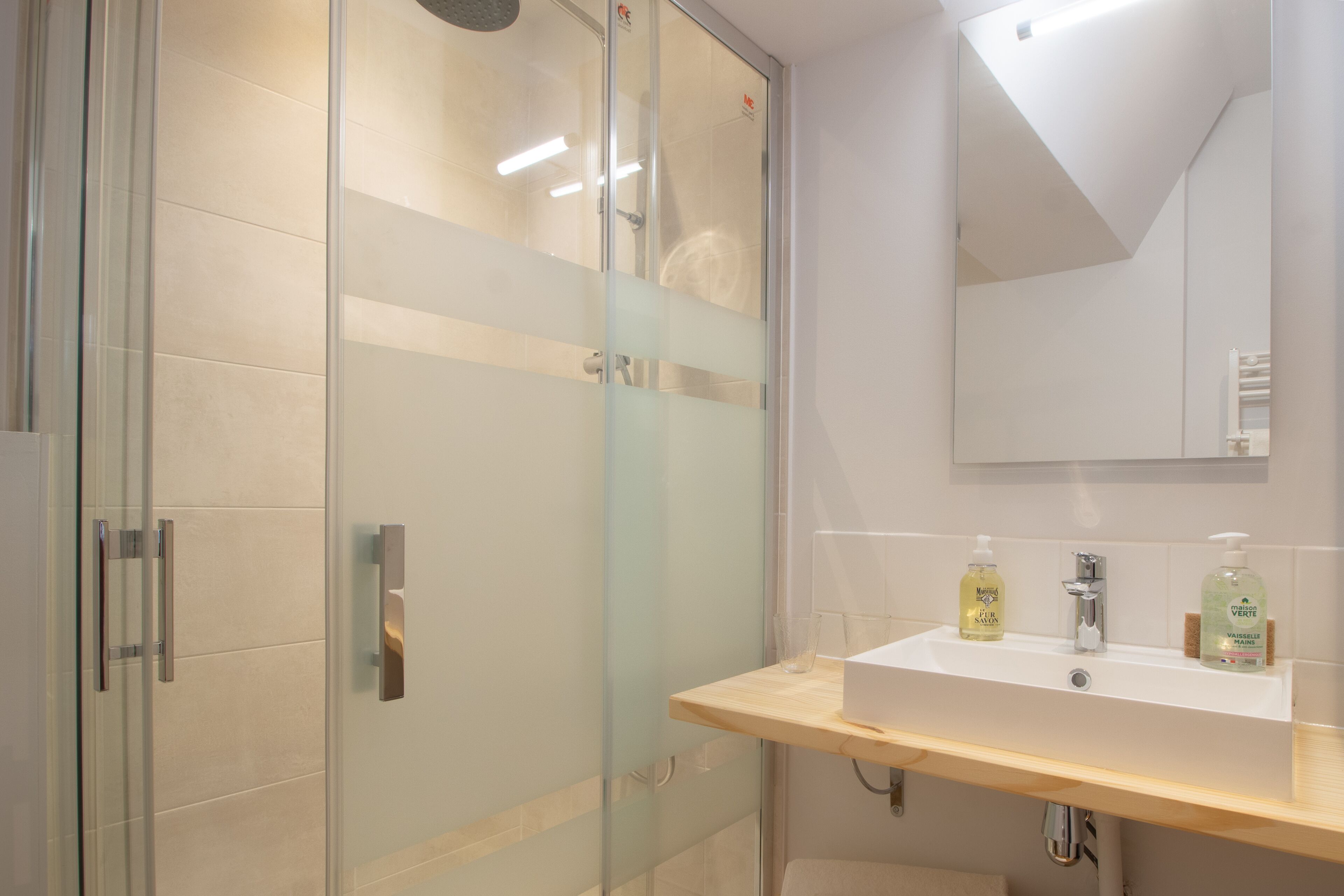 A modern bathroom with a glass shower enclosure, a wooden vanity with a sink, and a mirror above it.