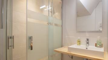 Ein modernes Badezimmer mit Duschkabine aus Glas, einem Holztischchen mit Waschbecken und einem Spiegel darüber.
