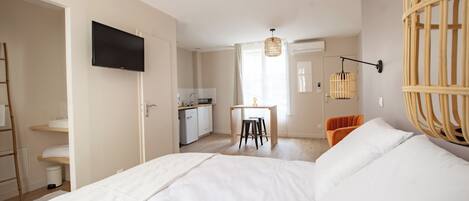 Un dormitorio con cama, televisión, zona de comedor y cocina.