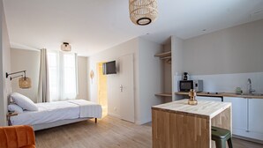 A modern bedroom with a bed, a small wooden table, and a kitchenette area. - Le Coursarlon (Bourges)