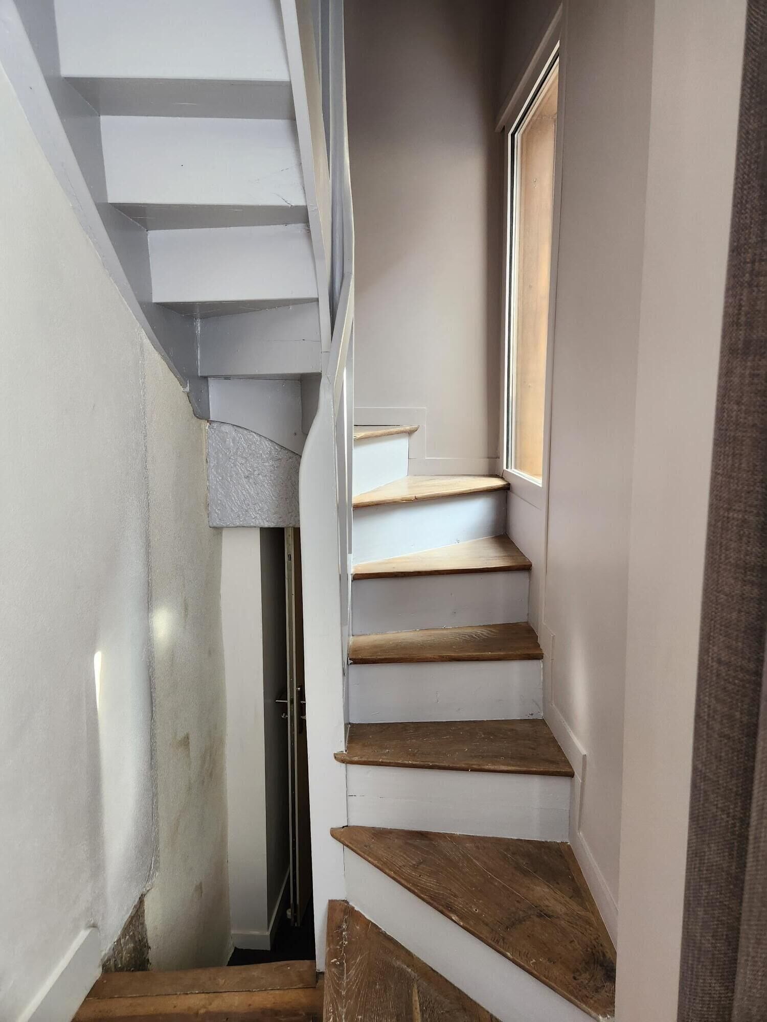 A narrow staircase with wooden steps and white walls, leading to a door at the top.