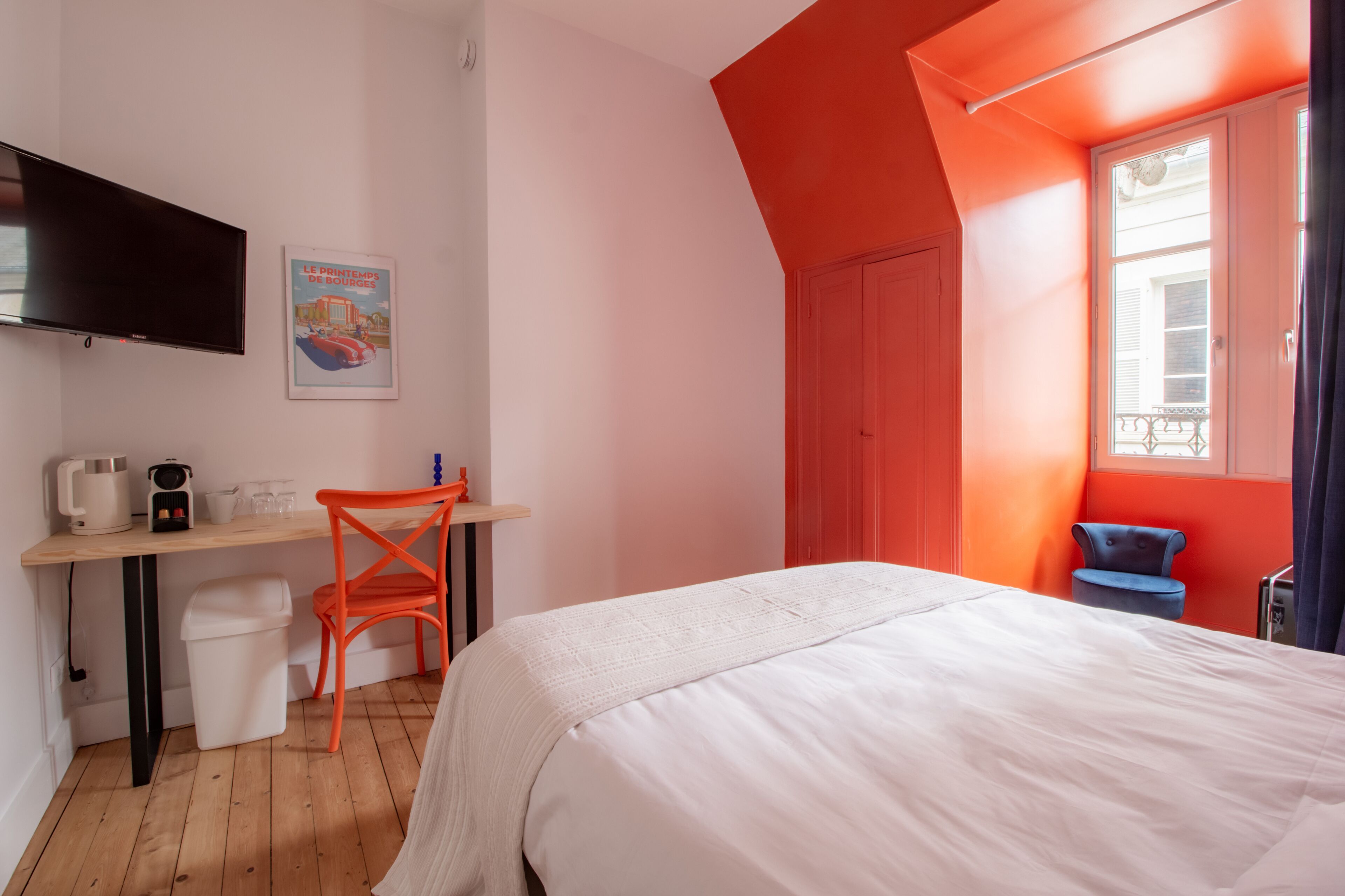A bedroom with a bed, a desk, a chair, a TV, and a window.