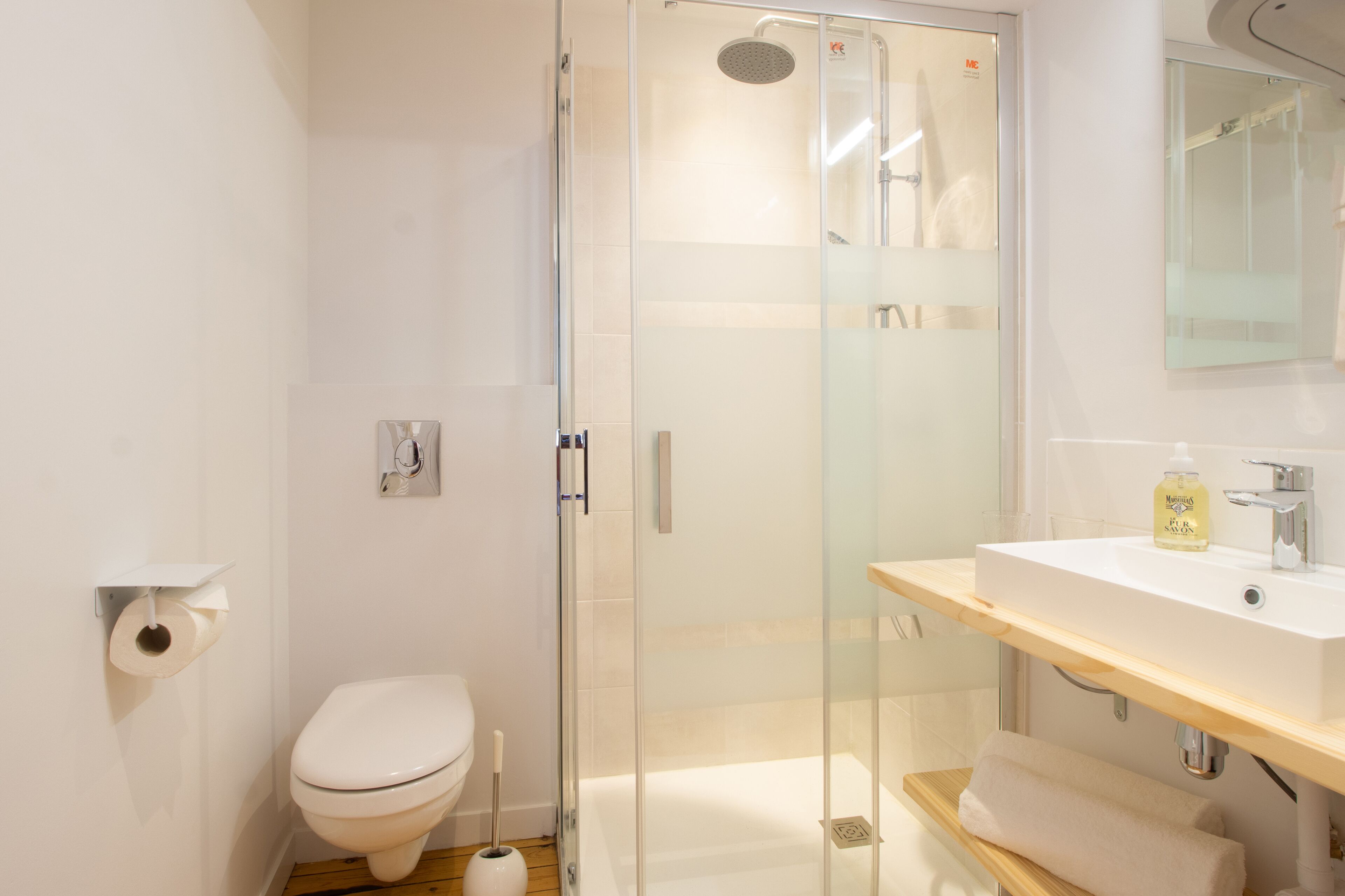 Ein modernes Badezimmer mit Duschkabine aus Glas, Toilette und Waschbecken mit Spiegel darüber.