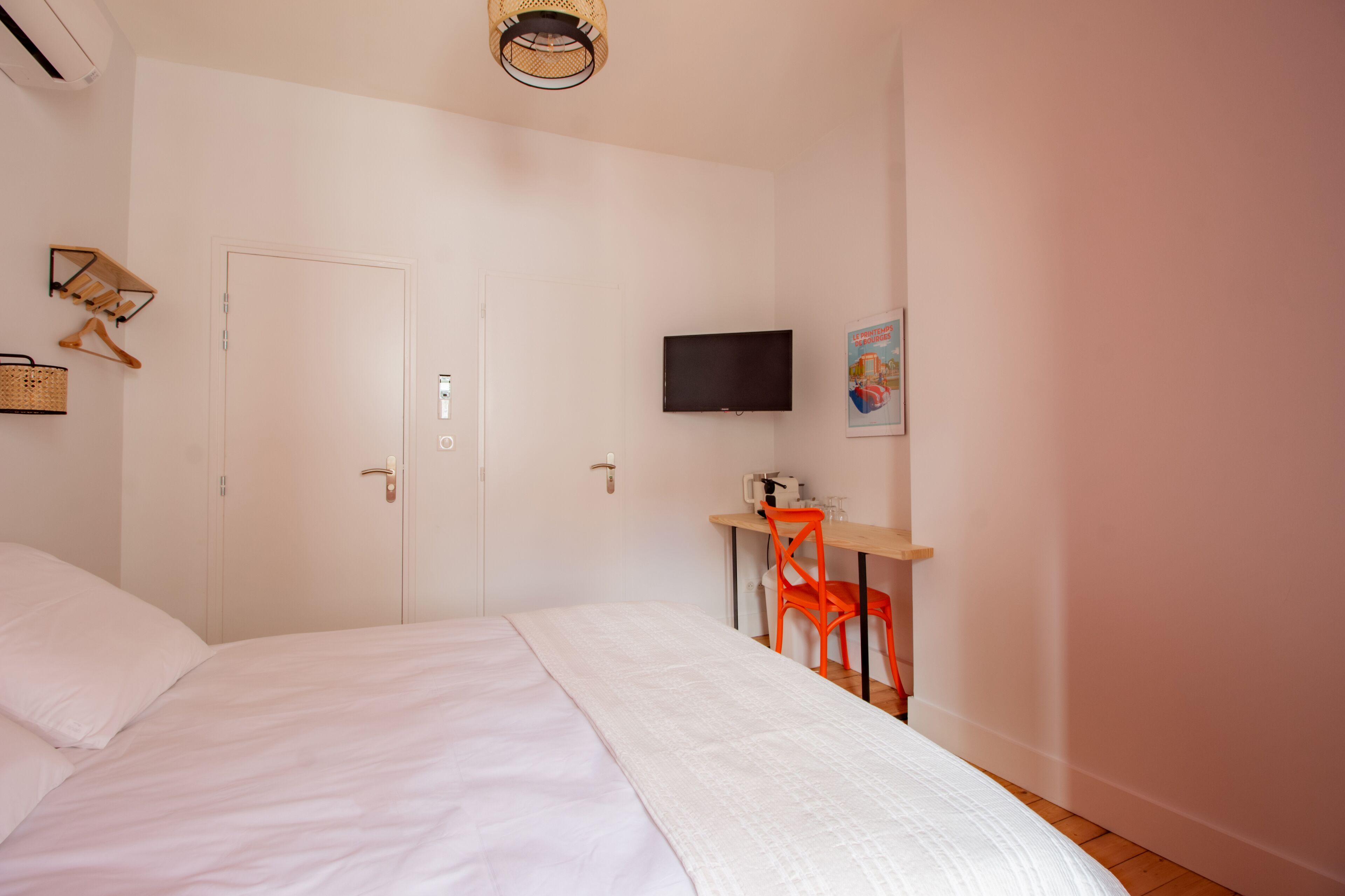 A bedroom with a bed, a desk with a chair, a television, and a door.