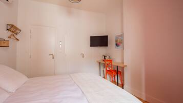 A bedroom with a bed, a desk with a chair, a television, and a door.