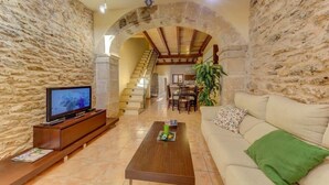 Una sala de estar con paredes de piedra, un mueble de madera para entretenimiento, un sofá, una mesa de centro y una escalera que conduce a un piso superior.