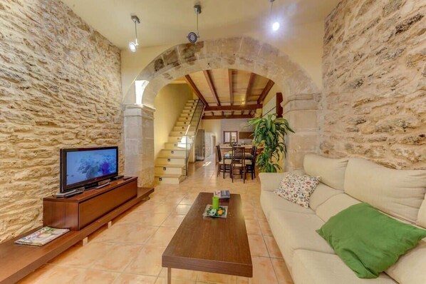 A living room with stone walls, a wooden entertainment unit, a sofa, a coffee table, and a staircase leading to an upper floor.