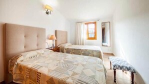 A bedroom with two beds, a nightstand, a lamp, a window with curtains, and a mirror. - Villa Viva Pollenca - Beautiful Stone built mallorcan villa (Pollenca)