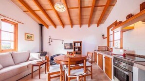 A cozy living room with a wooden dining table, a sofa, and a kitchen area with a stove and cabinets. - Villa Viva Pollenca - Beautiful Stone built mallorcan villa (Pollenca)