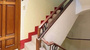 Una escalera con barandas de madera y una pared roja decorativa, que conduce a un piso superior.