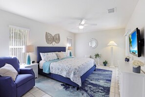 A bedroom with a bed, a chair, a desk, a television, and a ceiling fan.
