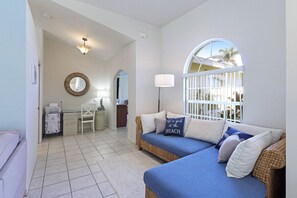 A room with a blue sofa, a desk, a chair, a mirror, and a window with a view of palm trees.