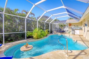 An indoor swimming pool with a glass enclosure, surrounded by palm trees and a patio area with outdoor furniture. - Walk to Beach! Family Retreat! (Marco Island)