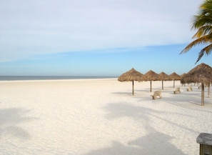 Ein Strand mit reetgedeckten Sonnenschirmen und Bänken, einem klaren Himmel und einem sandigen Ufer.