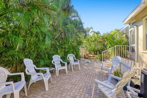 An outdoor patio with white plastic chairs and a brick floor, surrounded by lush greenery. - Walk to Beach! Family Retreat! (Marco Island)