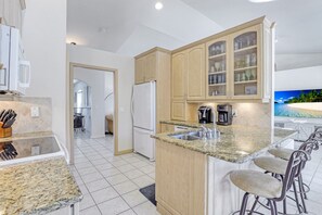 A modern kitchen with granite countertops, a built-in island with bar stools, and a view of a beach through a large window.