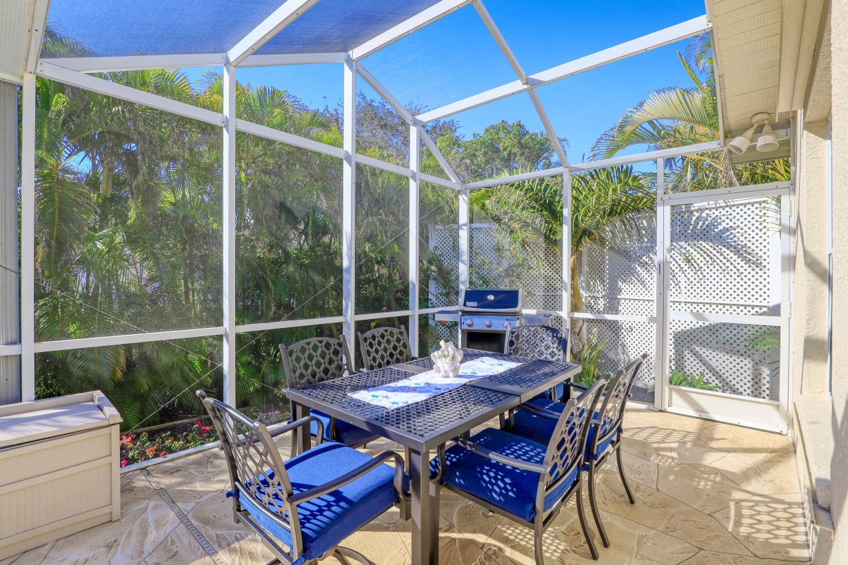 A covered patio area with a table and chairs, a grill, and a view of the surrounding greenery.