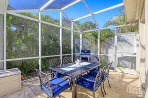 Ein überdachter Patio-Bereich mit Tisch und Stühlen, einem Grill und Blick ins umgebende Grün.
