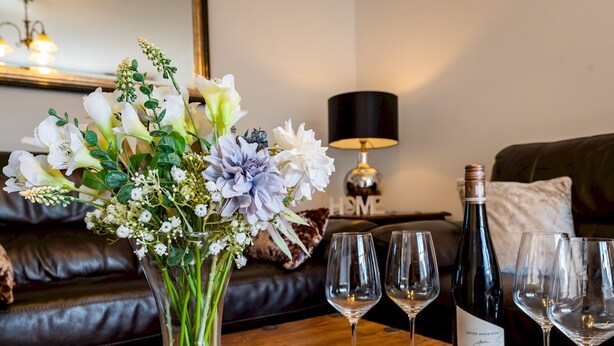 Une table en bois ornée d’un vase de fleurs, d’une bouteille de vin et de trois verres à vin.