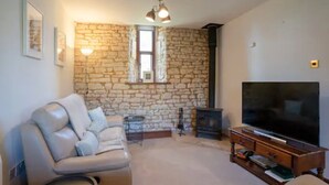 A living room with a stone wall, a leather sofa, a TV, and a fireplace. - Converted 17th century barn with garden parking - Pass the Keys (Cheltenham)
