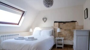 A bedroom with a bed, a nightstand, a lamp, a radiator, and a window. - Converted 17th century barn with garden parking - Pass the Keys (Cheltenham)