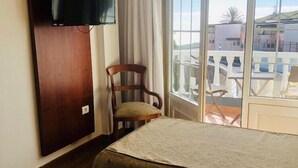 Habitación de hotel con cama, una silla, televisor montado en la pared y balcón con vistas a edificios.