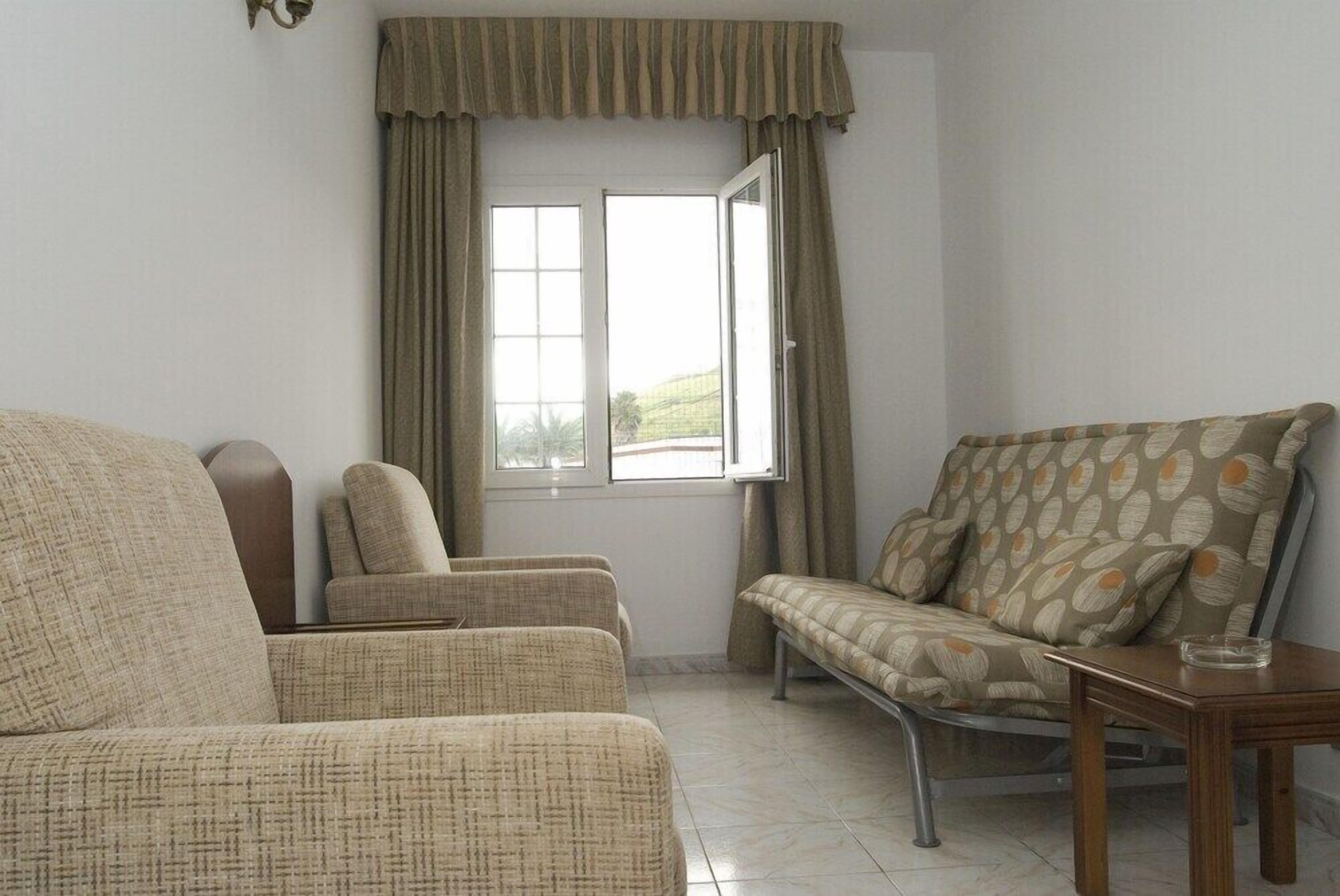 A room with a sofa, two armchairs, a small table, and a window with curtains.