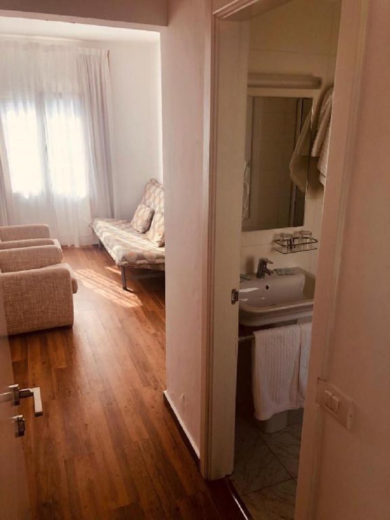A bedroom with a bed, a chair, a bathroom with a sink and mirror, and a wooden floor.
