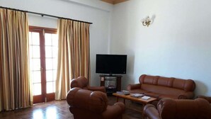 Una sala de estar con un sofá de cuero marrón, dos sillones, una mesa de centro y un televisor de pantalla plana.