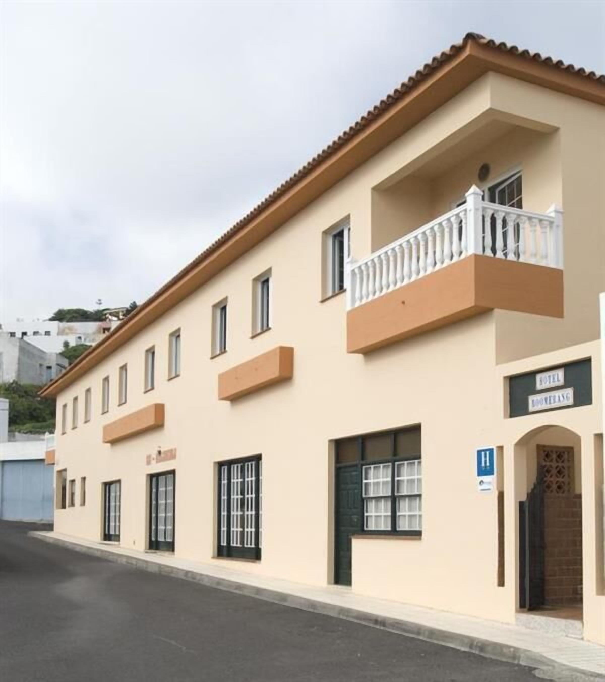 Un hotel de dos pisos con un balcón en el segundo nivel, un cartel que indica que es un hotel, y vista a la calle.