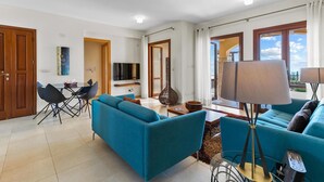 Un soggiorno moderno con un divano blu, un tavolo da pranzo con sedie, una televisione e una lampada.