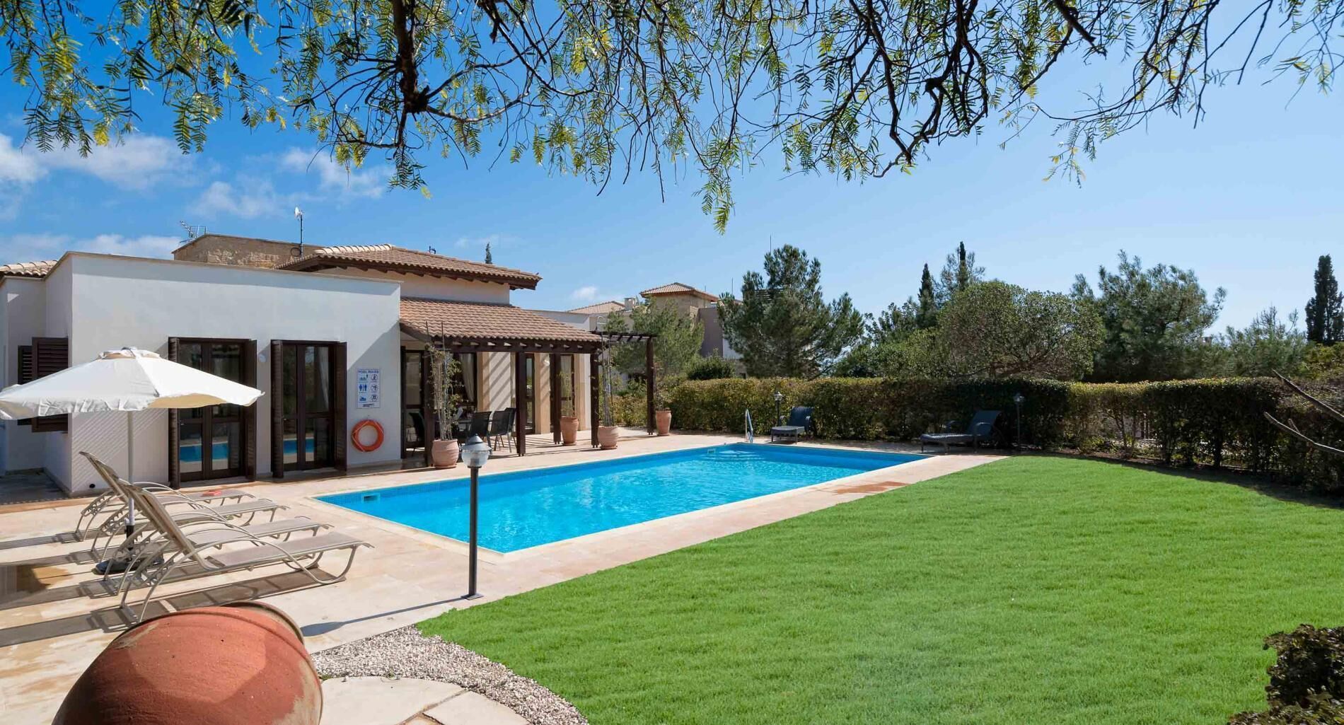 Una piscina con una pergola, un prato e un edificio con tetto in tegole.