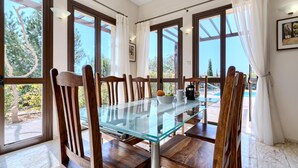 Un área de comedor con una mesa de vidrio, sillas de madera y ventanas amplias con vistas al exterior.