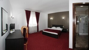 A hotel room with a bed, a desk, a chair, a TV, and a shower area. - Hotel Rebis International (Chiscani)