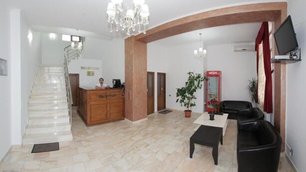 A hotel lobby with a reception desk, a staircase, a reception area, a seating area with a table and chairs, and a TV mounted on the wall. - Hotel Rebis International (Chiscani)