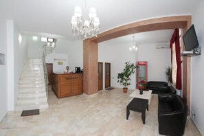 A hotel lobby with a reception desk, a staircase, a reception area, a seating area with a table and chairs, and a TV mounted on the wall. - Hotel Rebis International (Chiscani)