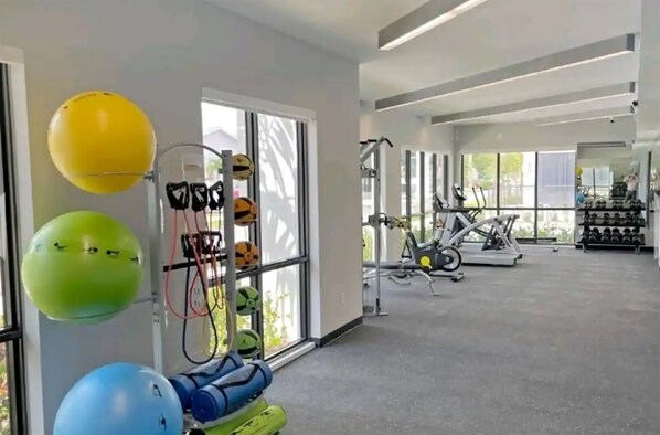 Un gimnasio con equipo de ejercicio, un estante de mancuernas y pelotas de ejercicio.