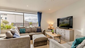 A modern living room with a sofa set, a TV, a small table with glasses, and a view of the outside. - 2 Bed in Woolacombe (oc-b27396) (Woolacombe)