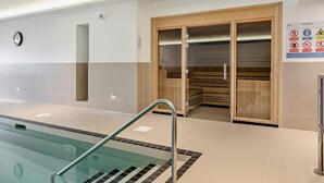 An indoor swimming pool with a glass barrier, wooden sauna doors, and a sign indicating pool depth. - 2 Bed in Woolacombe (oc-b27396) (Woolacombe)