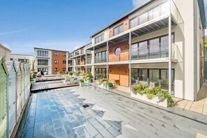 Un immeuble résidentiel moderne à plusieurs étages, doté d’une piscine sur le toit, d’un espace extérieur aménagé pour s’asseoir et de plantes en pot.