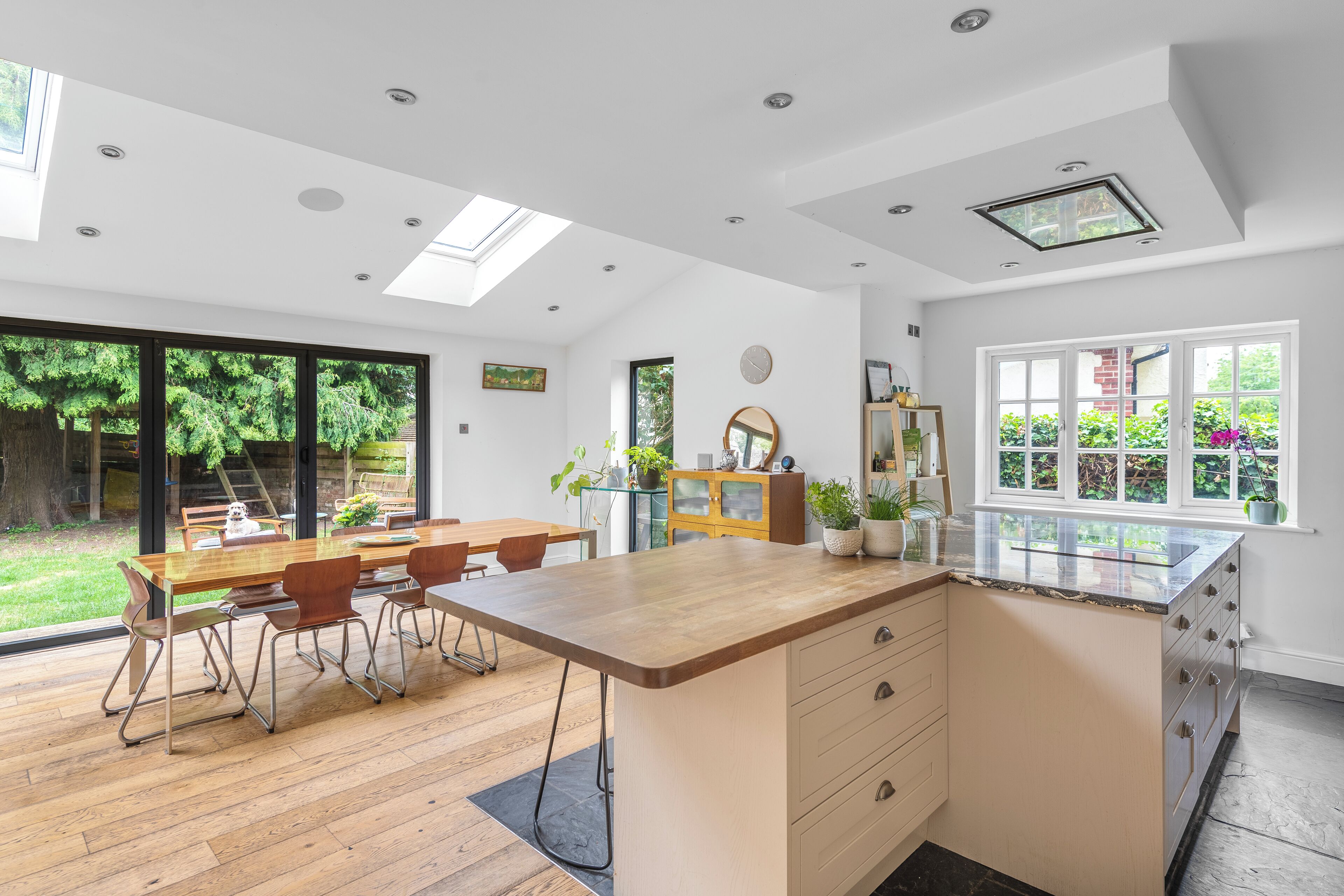 Una cocina moderna con una isla grande, suelo de madera y un comedor con mesa y sillas de vidrio.