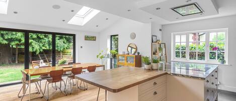 Una cocina moderna con una isla grande, suelo de madera y un comedor con mesa y sillas de vidrio.