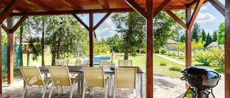 An outdoor patio with a wooden pergola, a barbecue grill, and a table with chairs.