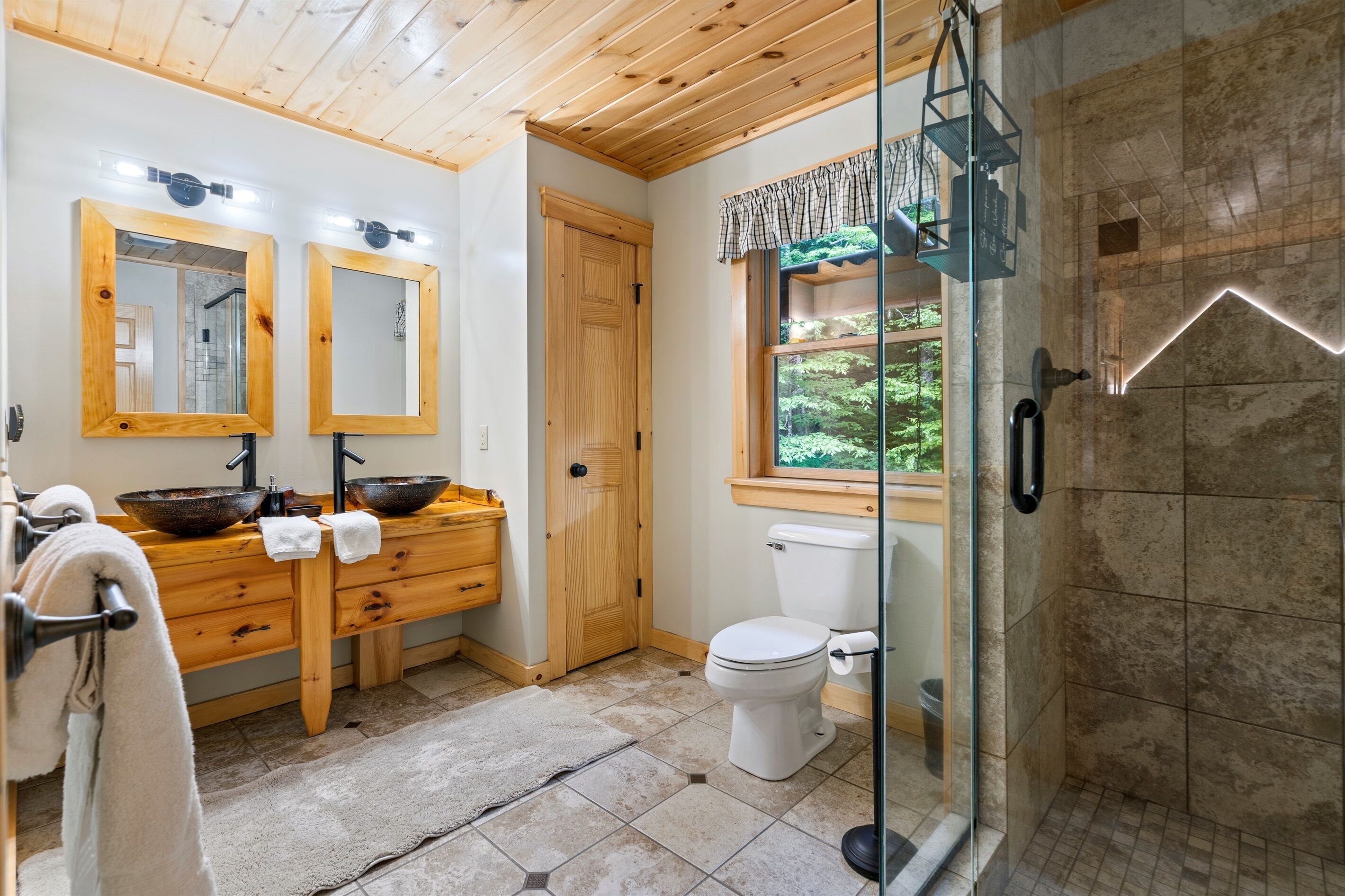 Une salle de bain avec des meubles en bois, deux vasques, des toilettes et une cabine de douche en verre.