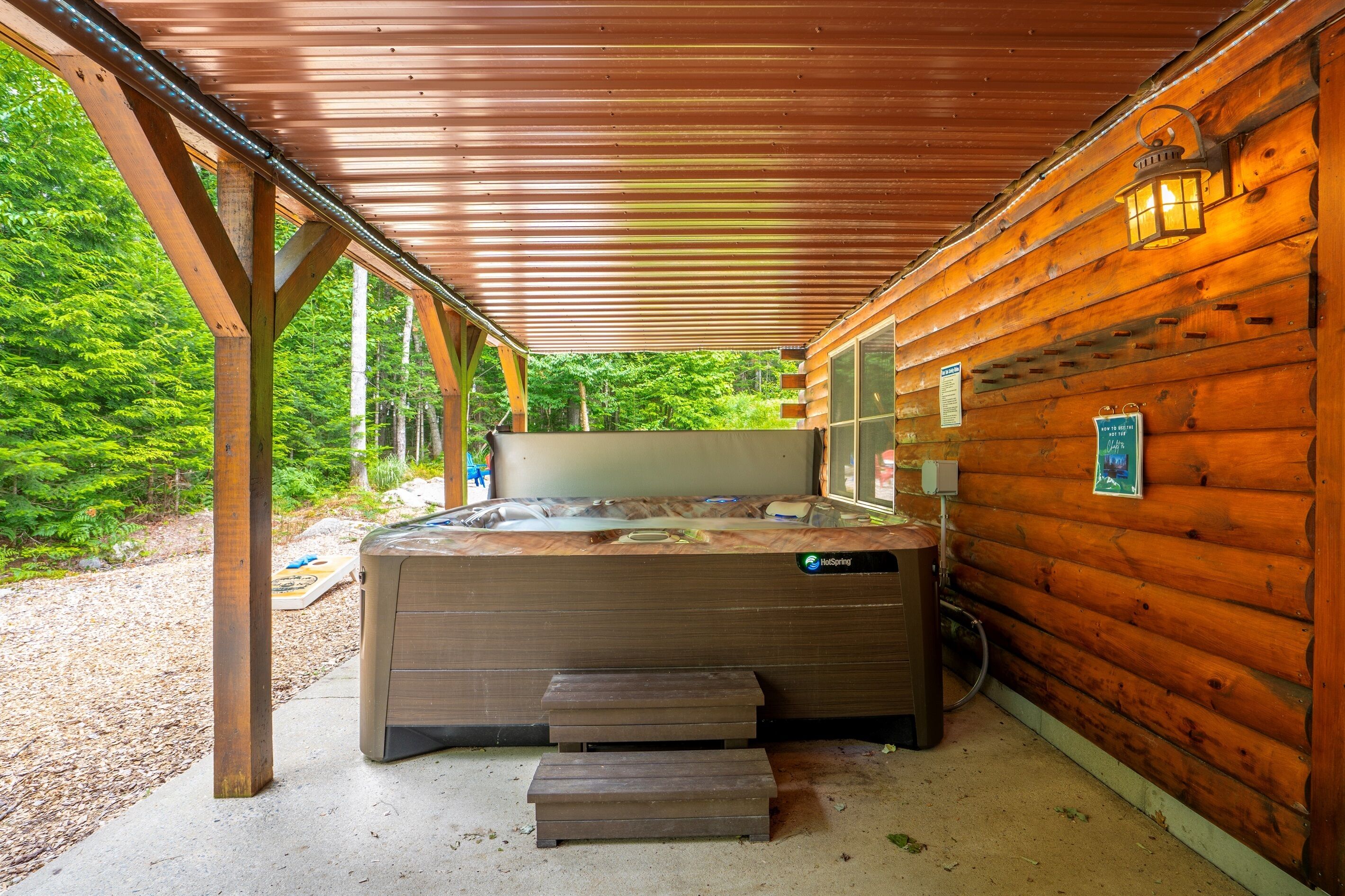 A hot tub in a wooden cabin with a covered patio, wooden steps, and a view of the forest.
