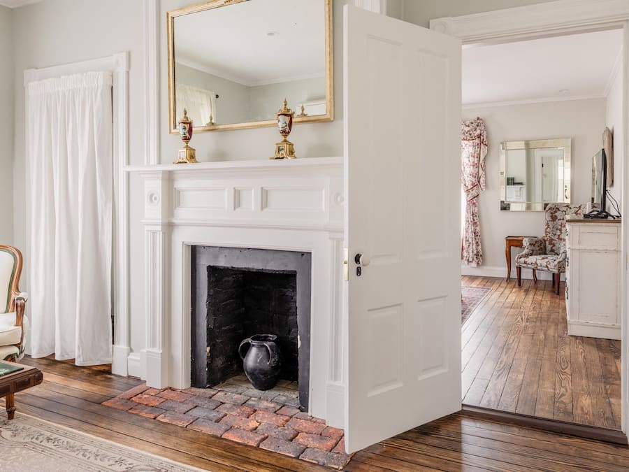 A room with a white fireplace, a mirror above it, and a door leading to another room.