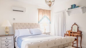 A bedroom with a large bed, a bedside table with a lamp, a dresser, and a mirror. - Armistead House (Williamsburg)